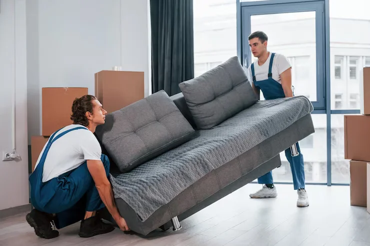carrying-heavy-sofa-two-young-movers-blue-uniform-working-indoors-room_146671-52051